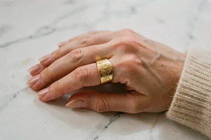 Main de femme portant une bague chevalière en or gravée posée sur marbre blanc, gros plan élégant