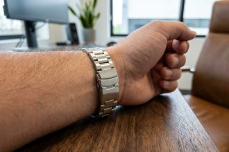Bracelet en acier inoxydable poli porté au poignet d'un homme sur un bureau en noyer